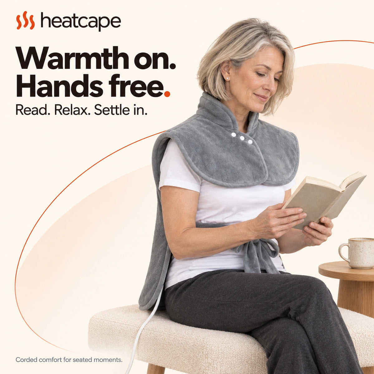 A man reading in an armchair wearing the wrap, cable visible beside the chair.