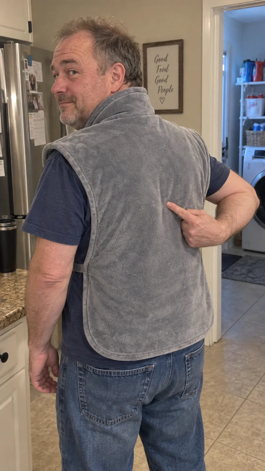 A man in his kitchen looking over his shoulder and pointing to his lower back, where the Heatcape back panel reaches.