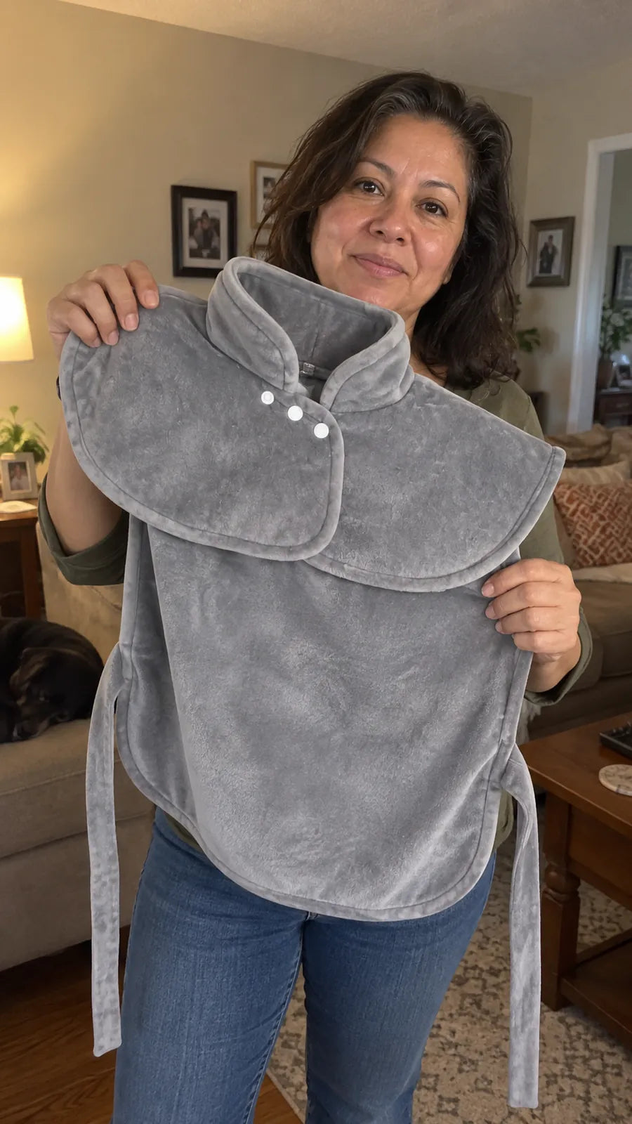 A woman in her living room holding up the Heatcape wrap to show its collar, snaps, back panel and ties.
